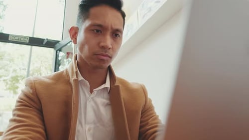Close-up of young businessman wearing beige suite working with laptop in cafe