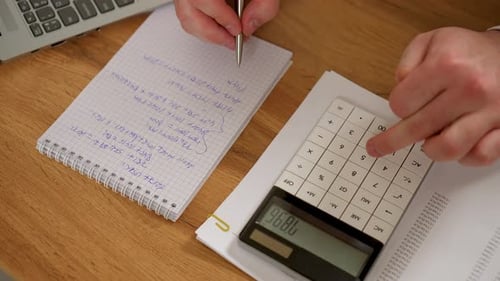 Mann macht Berechnungen auf dem Taschenrechner und macht sich Notizen mit Stift