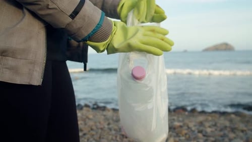 Primer plano de la mano de un voluntario que coloca una botella de plástico dentro de una bolsa de plástico en el mar