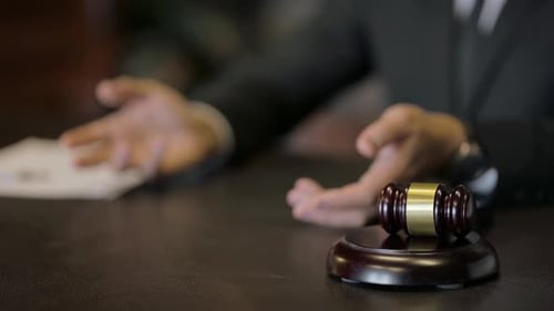 Primer plano de Gavel en la sala del tribunal con un gesto de hablar con las manos en segundo plano