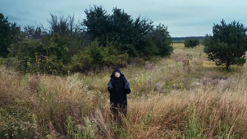 Scary death in black. Spooky figure in black mantle standing alone on the field near green trees.