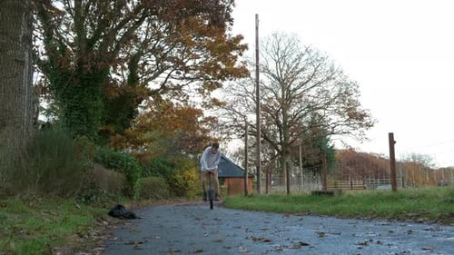 Young man performing unicycle tricks on a fall road surrounded by vibrant autumn trees
