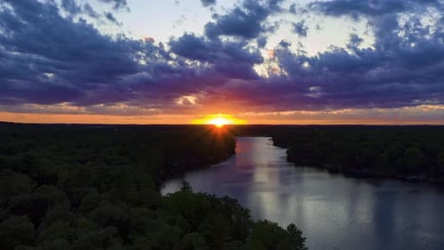 Golden Hour Sunset Glow Over a Calm Lake and a Silhouetted Forest, Aerial