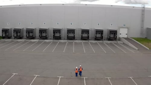 Engineers Walk Towards Warehouse Building with Open Gates