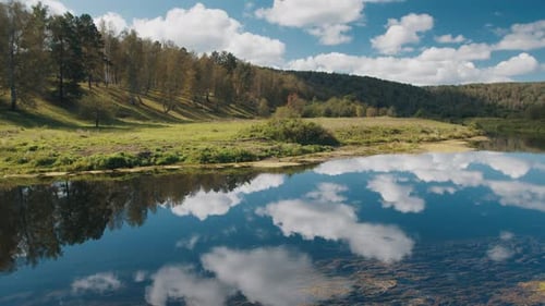 Calm River Flows in the Green Valley with Fluffy Clouds Reflecting on the Water Surface