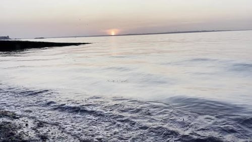 Wide shot showing the sun setting over the sea, showing the waves breaking on the beach.
