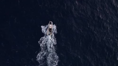 Aerial view of boat near rocky cliffs by clear blue sea, Spain.