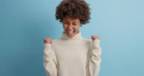 Excited Woman Cheerfully Pumping Fists Against Blue Background