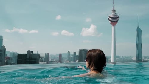 Woman in Infinity Pool Enjoying City Skyline View with Iconic Tower