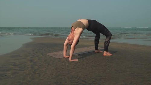 Mujer caucásica de yoga en pantalones de chándal se estira hacia atrás en una playa tranquila