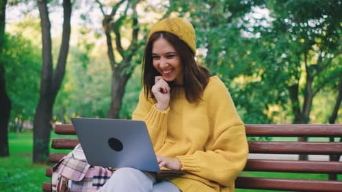 A Joyful Woman Working on Her Laptop in a Beautiful Park Setting Filled with Lush Greenery and