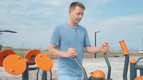 Young Male Doing Cardio Workout Exercises on Elliptical Trainer in a Street Gym Active Man