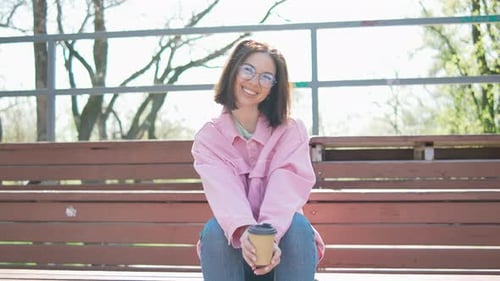 Mulher de óculos e jaqueta rosa gosta de café na manhã ensolarada ao ar livre