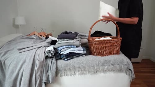 Adult Sorting Clothing in Bedroom Putting in Basket