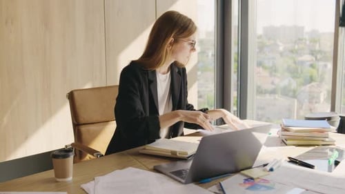 Businesswoman in Glasses and Suit Working in the Office with Important Documents and Laptop Writes