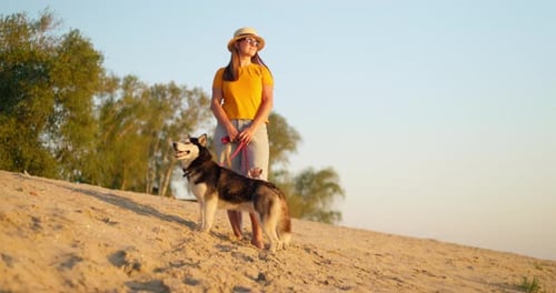Young Woman Enjoying Evening Walk with Her Pet Dog on the Beach in Summer