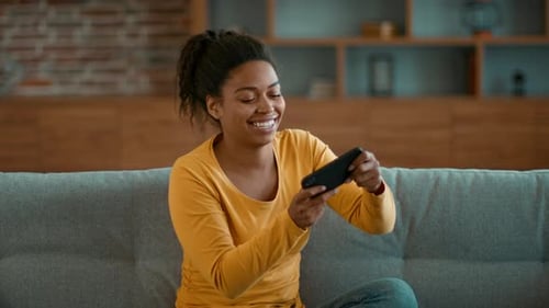 Smiling Woman Plays Game on Mobile Phone at Home