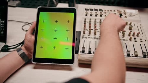 professional recording studio sound engineer holding tablet with green screen near equalizer mixer