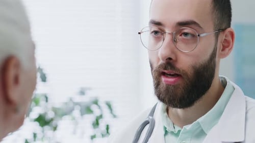 Friendly Doctor Talking With Elderly Patient in Medical Clinic