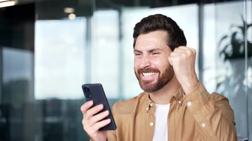 Happy excited handsome businessman received great news on mobile phone in business office. Smiling