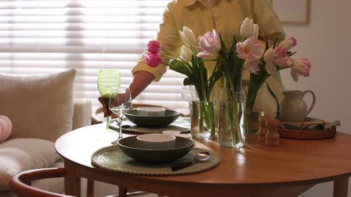 Woman Setting Dining Table with Fresh Tulips in Sunlit Home