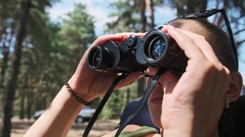 Woman Looks Through Binoculars on a Chaise Longue in a Forest Near Camping