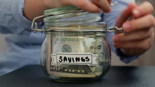 Unerkennbare Frau fügt Geld zum Sparen in einem mit Dollar-Banknoten gefüllten Glasgefäß hinzu ERSPARNISSE