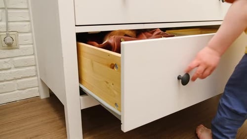 Child Opens a White Chest of Drawers
