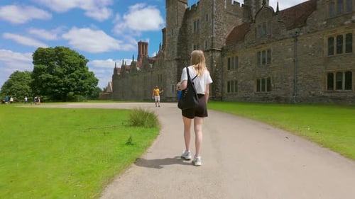 Group of People Walking on a Path Near a Castle in a Green Field Under a Clear Blue Sky During the