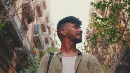 Close up, young smiling man walks along the narrow street of the old city and looks around