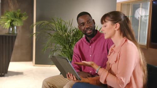 Discussing work, multiracial colleagues using tablet and talking in modern office setting