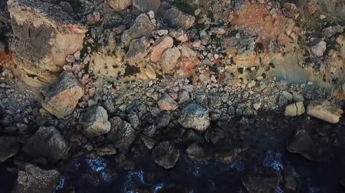 Drone shot of a rocky landscape in Malta, panning downward towards the blue, clear ocean.