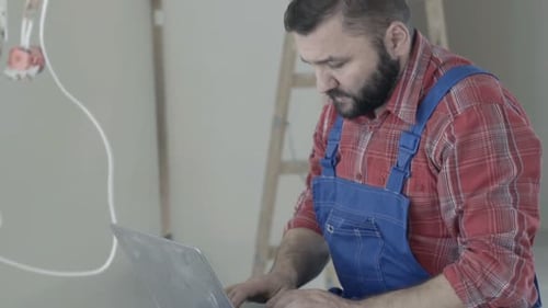 Construction Worker Uses Laptop in Unfinished Room
