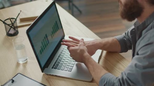 Man Examines Rising Bar Graphs on a Laptop