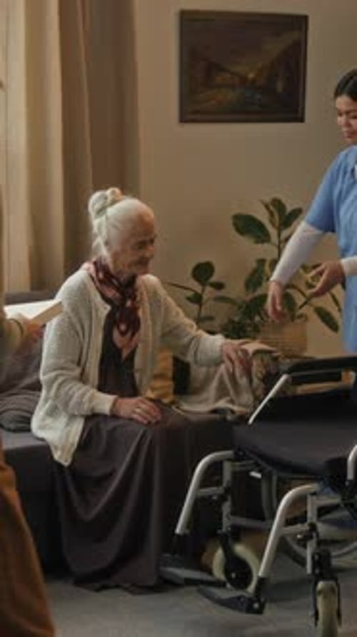 Female Caregiver Helping Senior Woman Into Wheelchair