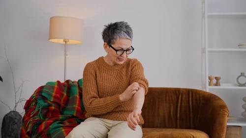 Stressed Senior Woman Scratching Itchy Skin Allergy on Her Arm at Home