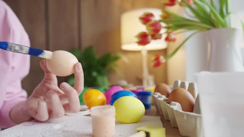 Woman painting Easter egg at home with pastel paints