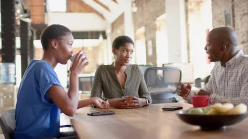Happy african american colleagues talking and drinking coffee in creative office, slow motion