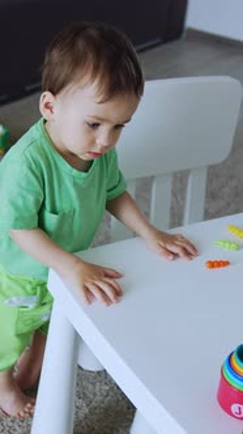 Adorable niño pequeño de pie cerca del escritorio blanco. Un niño hermoso pone pequeños juguetes en colores