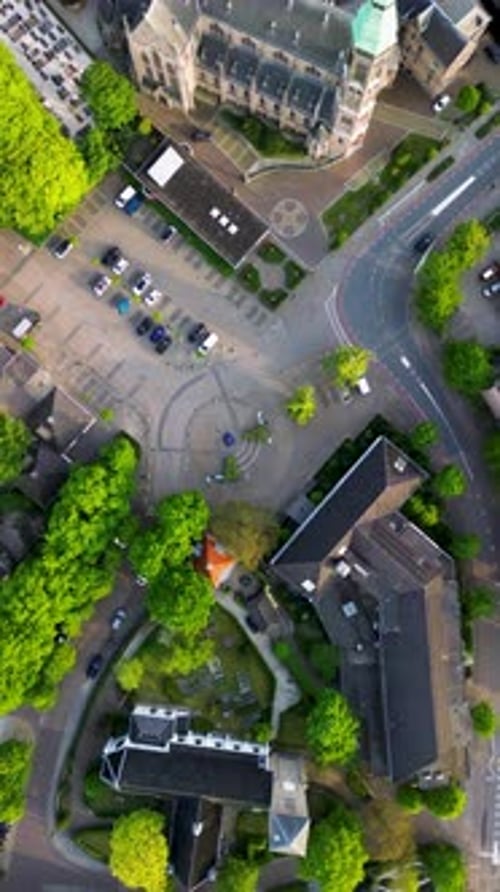 Aerial view of town plaza with circular paving, bollards, planters pitched roof buildings and parked