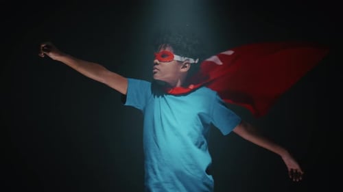 Studio Shot of Little Boy in Cape and Mask Posing Like Flying Superhero
