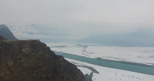 Aerial view of snowy mountain, river, and cliff in winter, Pakistan.