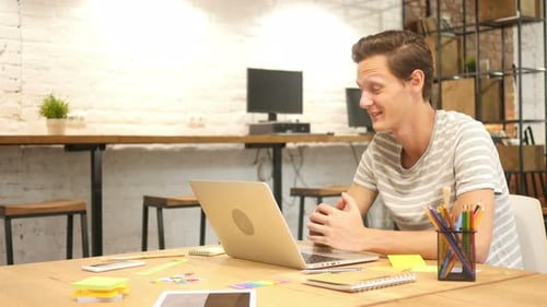 Young Man Talking on Video Call on Laptop in Office