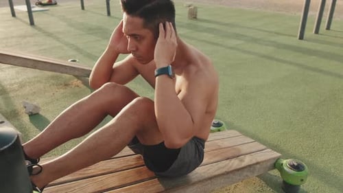 Young man exercising abdominal muscles on the sports ground outside
