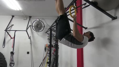 Dark-haired man with beard does pull-ups in the fitness basement