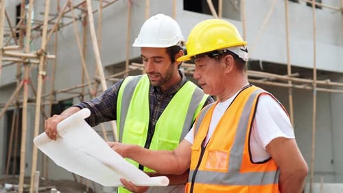 Two Construction Workers Reviewing Blueprint at Construction Site