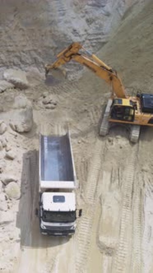 Aerial view of excavator filling truck with sand