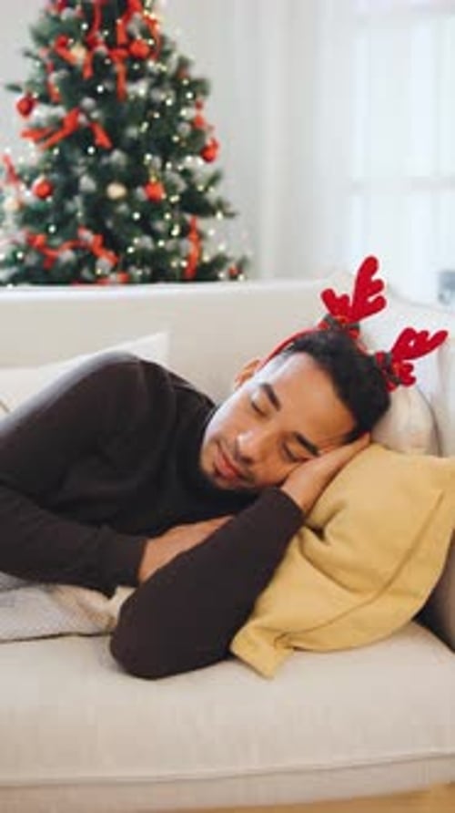 Man with Antlers Peacefully Sleeps on the Couch While a Decorated Christmas Tree Glows Softly in the