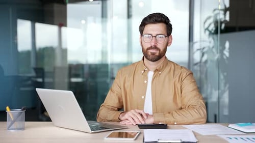 Portrait of happy businessman sitting at desk at workplace in modern business office. Confident