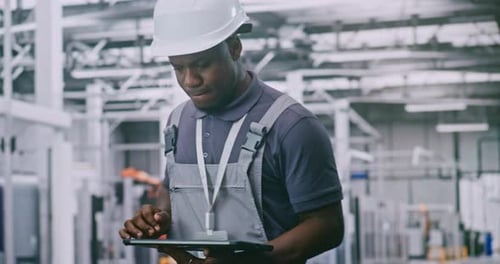 Professional Factory Employee Supervises Robotic Machinery Using Mobile Control Device